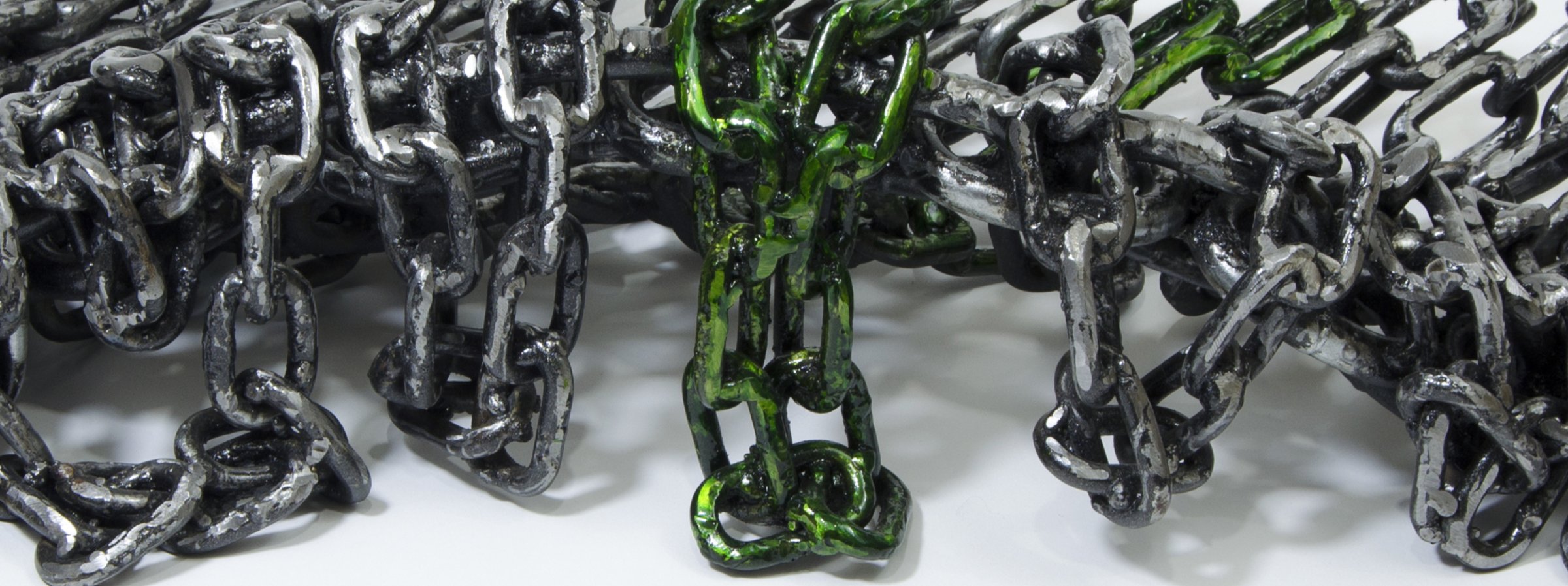 Dettaglio macro delle catene metalliche riciclate, con un elemento verniciato di verde